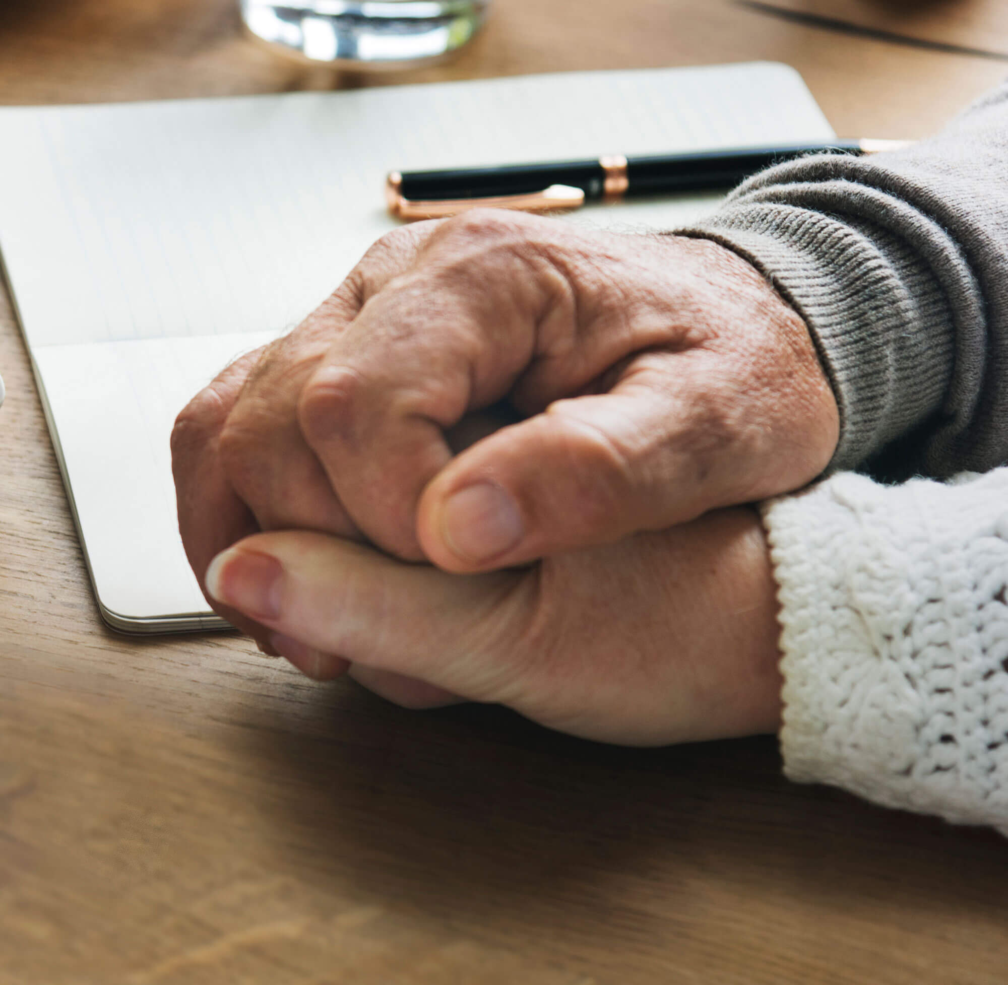 Elderly male and female hands holding each other over top of a note pad.